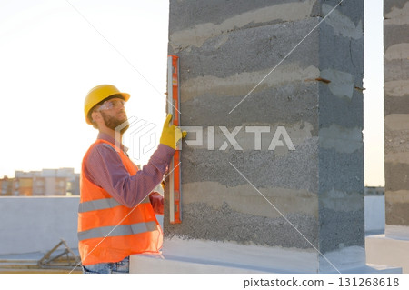 Construction worker using spirit level on building site at sunset Construction worker using spirit level on building site at sunset 131268618