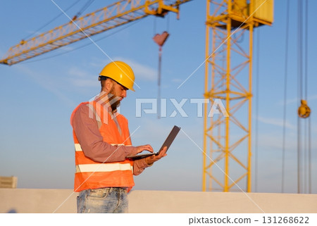 Construction engineer using laptop at building site with crane in background Construction engineer using laptop at building site with crane in background 131268622