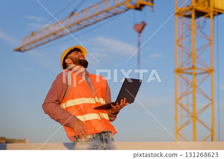 Construction engineer using laptop at building site with crane in background 131268623