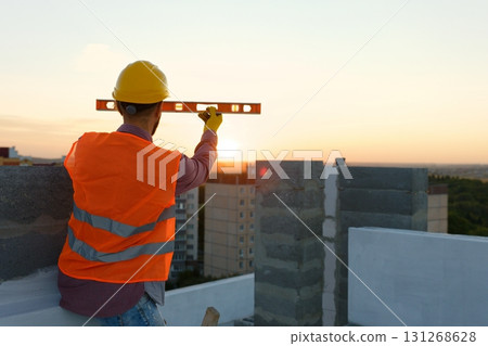 Construction worker using spirit level at building site with crane in background 131268628