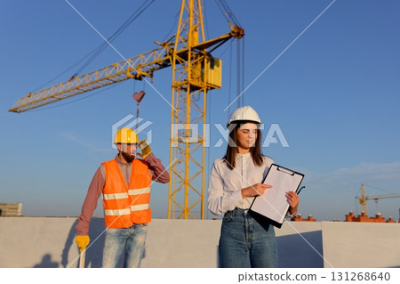 Female engineer showing a document to a construction worker on a rooftop Female engineer showing a document to a construction worker on a rooftop 131268640
