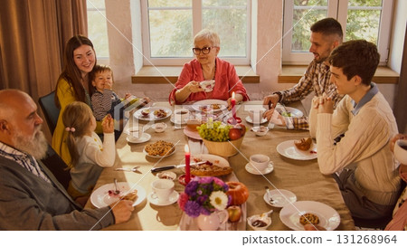 Family gathering around table sharing tea and pastries in warm atmosphere 131268964