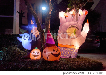 Bright inflatables show ghosts, a haunted tree, and a giant hand with an eyeball. Cheerful glowing pumpkins create a playful night yard scene. Bright inflatables show ghosts, a haunted tree, and a giant hand with an eyeball. Cheerful glowing pumpkins create a playful night yard scene. 131269405