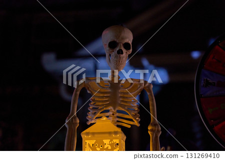 Small skeleton stands behind a glowing lantern at night. Spooky yard decoration with dark background and dramatic light. Small skeleton stands behind a glowing lantern at night. Spooky yard decoration with dark background and dramatic light. 131269410