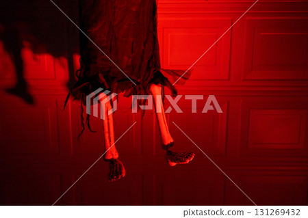 Tattered black fabric reveals bony legs and feet hanging in intense red light. Spooky Halloween decoration with strong shadows, copy space, and dramatic mood. 131269432