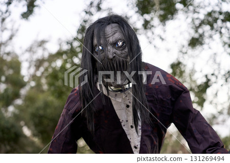 A horrific gray-faced creature with glowing blue eyes leans forward through long hair. Tattered clothing, sharp teeth, and chains suggest a terrifying captive. 131269494