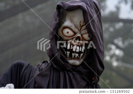 A hooded skeleton reaper stares with red glowing eyes and a wide grin. Black robe, bone details, and sharp teeth create a creepy Halloween close-up portrait. A hooded skeleton reaper stares with red glowing eyes and a wide grin. Black robe, bone details, and sharp teeth create a creepy Halloween close-up portrait. 131269502