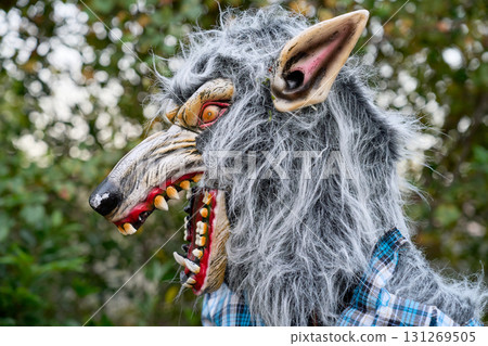 Side profile of a snarling werewolf with gray shaggy fur and sharp teeth. The long muzzle, pointed ear, and glowing red-yellow eye stand out in an outdoor yard scene. Side profile of a snarling werewolf with gray shaggy fur and sharp teeth. The long muzzle, pointed ear, and glowing red-yellow eye stand out in an outdoor yard scene. 131269505