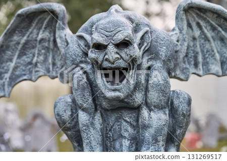 A detailed view of a winged stone gargoyle with an open mouth and sharp teeth. Weathered texture and gothic style make a scary Halloween decoration. 131269517