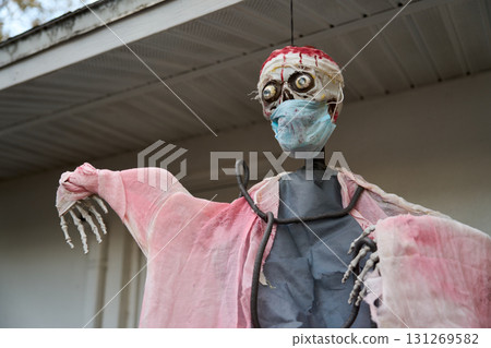 Grim skeleton figure in tattered pink robe wears a stained face mask and head wrap. Spooky hospital-inspired Halloween decoration displayed outside a home. 131269582