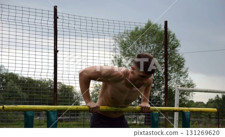 Male shirtless athlete doing push ups on parallel bars at nature. Strong sporty man exercising at sports ground. Young sportsman training hard outdoor. Concept of active sportive lifestyle. Slow mo Male shirtless athlete doing push ups on parallel bars at nature. Strong sporty man exercising at sports ground. Young sportsman training hard outdoor. Concept of active sportive lifestyle. Slow mo 131269620