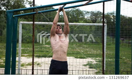 Young muscular sportsman doing pull ups at sports ground. Athletic guy exercising outdoor. Strong sporty man working out at summer nature. Concept of healthy and active lifestyle. Slow motion 131269637