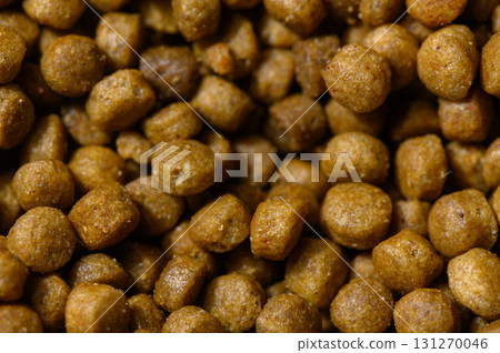Pet food granules scattered on a surface, showcasing their round, textured forms in warm lighting 131270046