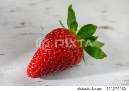Freshly picked strawberry resting on a rustic wooden surface in soft lighting 131270080