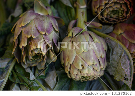 Fresh artichokes resting on leafy green layers at the local market during vibrant morning hours 131270162
