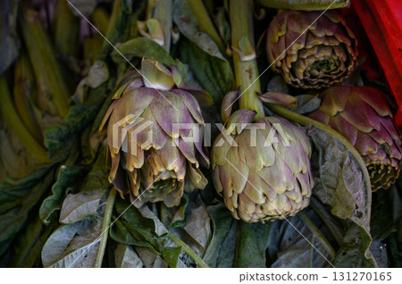 Freshly harvested artichokes hanging at a vibrant market stall in the early morning sun 131270165