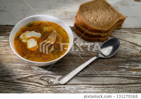 Warm bowl of hearty soup served with sliced brown bread on a rustic wooden table 131270168