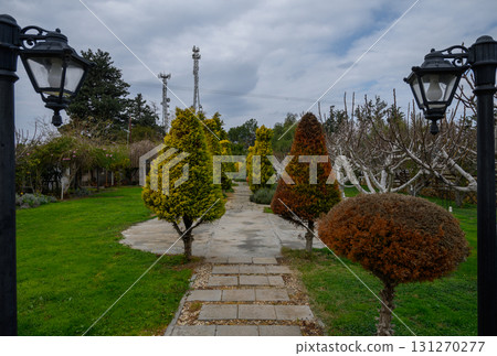 Serene pathway lined with trees leading to a tranquil garden under a cloudy sky 131270277