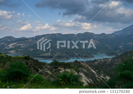 Breathtaking view of rolling hills and turquoise waters under a cloudy sky Breathtaking view of rolling hills and turquoise waters under a cloudy sky 131270280
