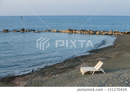 Lone lounge chair by calm sea creates serene atmosphere at twilight on a peaceful beach 131270426