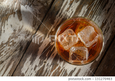 Refreshing drink with ice cubes resting on rustic wooden surface during golden 131270463