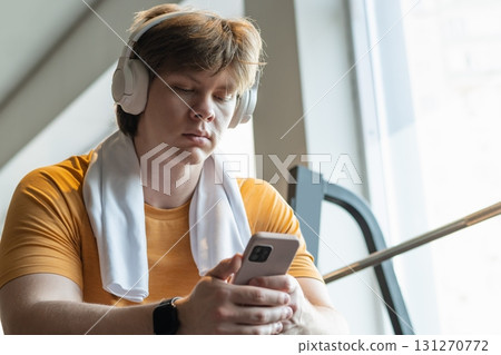Sporty caucasian man relax and sitting with mobile phone, listen music headphones and texting at gym. Bodybuilder during training. Sporty caucasian man relax and sitting with mobile phone, listen music headphones and texting at gym. Bodybuilder during training. 131270772