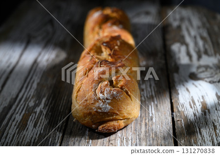 Rustic loaf of bread resting on weathered wooden table under soft light Rustic loaf of bread resting on weathered wooden table under soft light 131270838