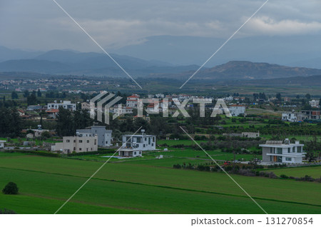 Green fields and modern homes amidst a cloudy sky in a tranquil rural landscape Green fields and modern homes amidst a cloudy sky in a tranquil rural landscape 131270854