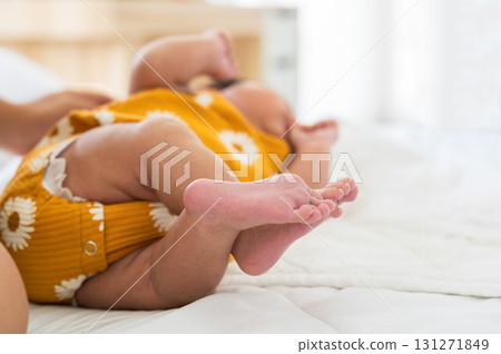 Newborn baby wearing yellow onesie lying on soft white bed with focus on tiny pink feet Newborn baby wearing yellow onesie lying on soft white bed with focus on tiny pink feet 131271849
