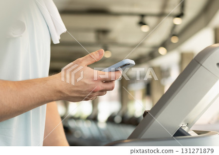 Sporty fit young man with mobile phone checking apps and fitness progress on running track. Athlete warm up on treadmill at gym. Close up. Sporty fit young man with mobile phone checking apps and fitness progress on running track. Athlete warm up on treadmill at gym. Close up. 131271879