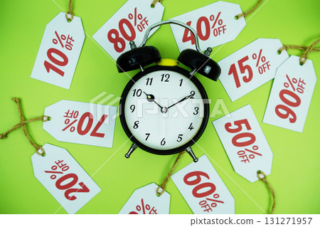 Clock surrounded by various discount tags with percentages like 10%, 20%, 30%, up to 90% off, set against a bright green background 131271957