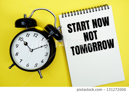 Start Now Not Tomorrow text with alarm clock flat lay on yellow background 131272008