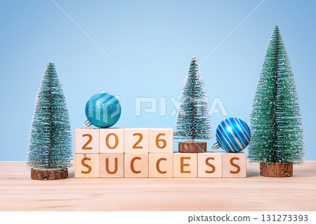 New Year 2026 and Christmas postcard. Wooden cubes with numbers 2026 and word success and green Christmas trees on a wooden table and a blue background. New Year 2026 and Christmas postcard. Wooden cubes with numbers 2026 and word success and green Christmas trees on a wooden table and a blue background. 131273393