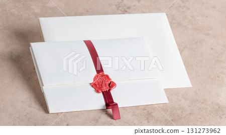 White envelope sealed with red ribbon and on beige stone background 131273962