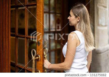 Woman opens wooden door and enters from street into interior of building. 131275082