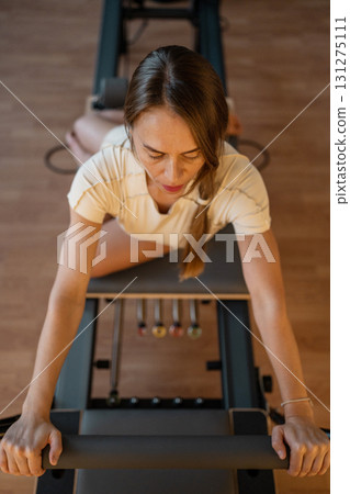 Woman doing Swan exercise on Pilates Reformer for the chest and back muscles, focusing on flexibility, strength, and control with determination 131275111