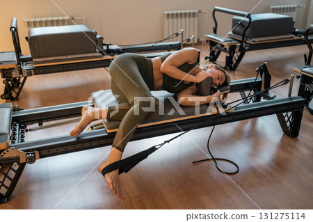 Tired and happy woman practices Pilates on reformer equipment, showcasing her flexibility and strength dynamically 131275114