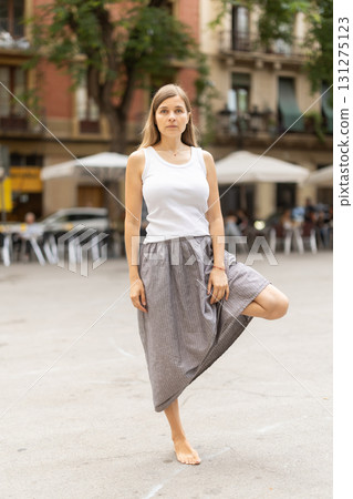 Woman in midst of bustle of city in pose of tree asana 131275123