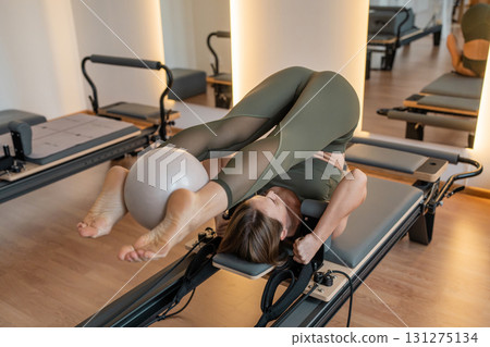 Woman doing Pilates exercise for core and back muscles on Reformer machine with determination and focus on strength body 131275134