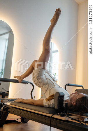 Woman training on the reformer bed at Glute bridge Pilates workout. Reformer pilates studio machine for fitness workouts in gym. Fit, healthy and strong authentical body. Fitness concept Woman training on the reformer bed at Glute bridge Pilates workout. Reformer pilates studio machine for fitness workouts in gym. Fit, healthy and strong authentical body. Fitness concept 131275142