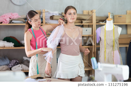 Adult female seamstress adjusting clothes on young woman Adult female seamstress adjusting clothes on young woman 131275196