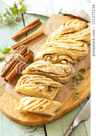 Braided cinnamon sweet bread on rustic wooden board with cinnamon sticks and herbs. Braided cinnamon sweet bread on rustic wooden board with cinnamon sticks and herbs. 131275216