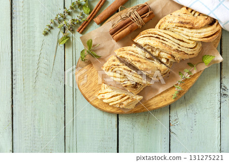 Braided cinnamon sweet bread on rustic wooden board with cinnamon sticks and herbs. Top view flat lay background. Copy space. Braided cinnamon sweet bread on rustic wooden board with cinnamon sticks and herbs. Top view flat lay background. Copy space. 131275221