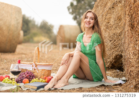 Portrait of woman in green dress with basket of fruits on picnic in farm field 131275319