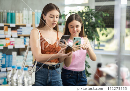 Mother and daughter in a summer dress choose cough syrup in pharmacy 131275333