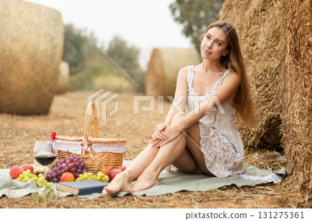 Pretty woman in white dress sitting near haystack on picnic 131275361