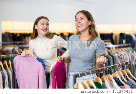 Happy young women holding winter jumpers and sweaters on racks during shopping in a boutique 131275431