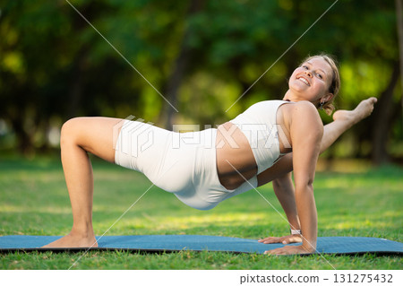 Girl in park on green grass of lawn performs purvottanasana 131275432