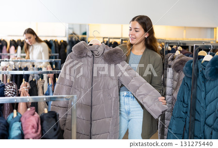Dreamy female choosing warm winter jacket while shopping in a clothing store 131275440
