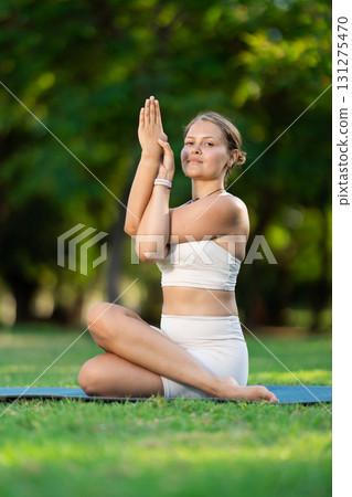 Girl doing Gomukhasana Garudasana yoga pose in summer park 131275470